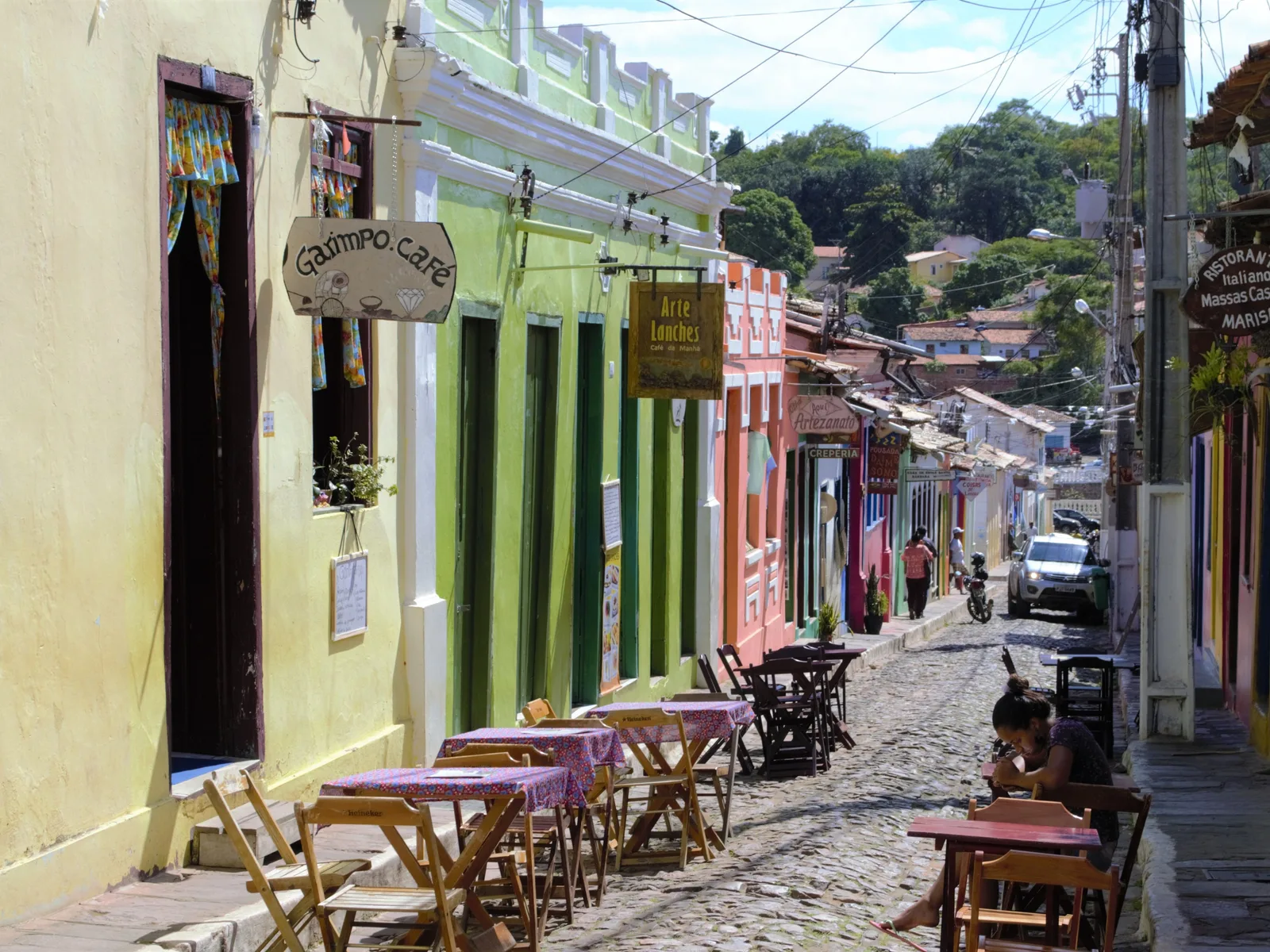 A cobbled street in Lençóis, the town in Bahia, lined with painted shopfronts, awnings and café tables