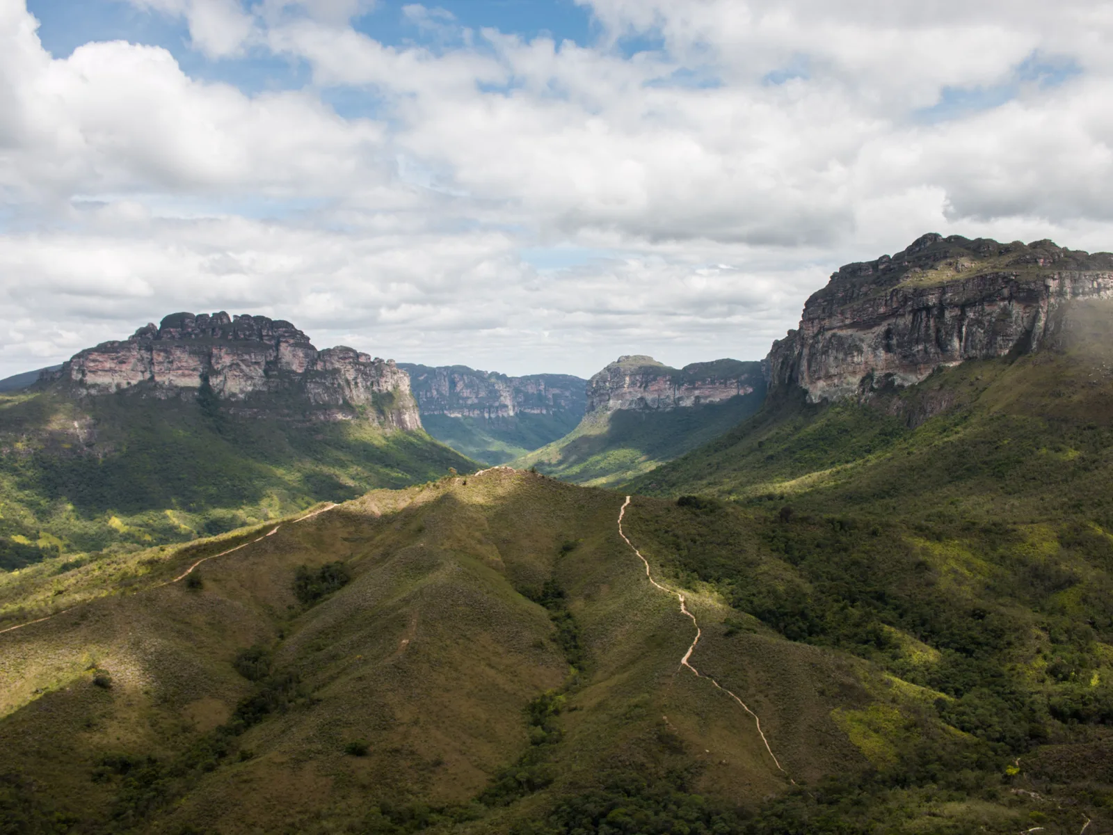 A green valley floor in the Chapada Diamantina with a footpath winding through it between long flat-topped escarpments