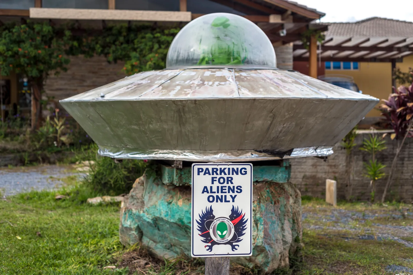 A silver flying-saucer sculpture with a green dome on a rock pedestal, with a sign reading Parking for aliens only