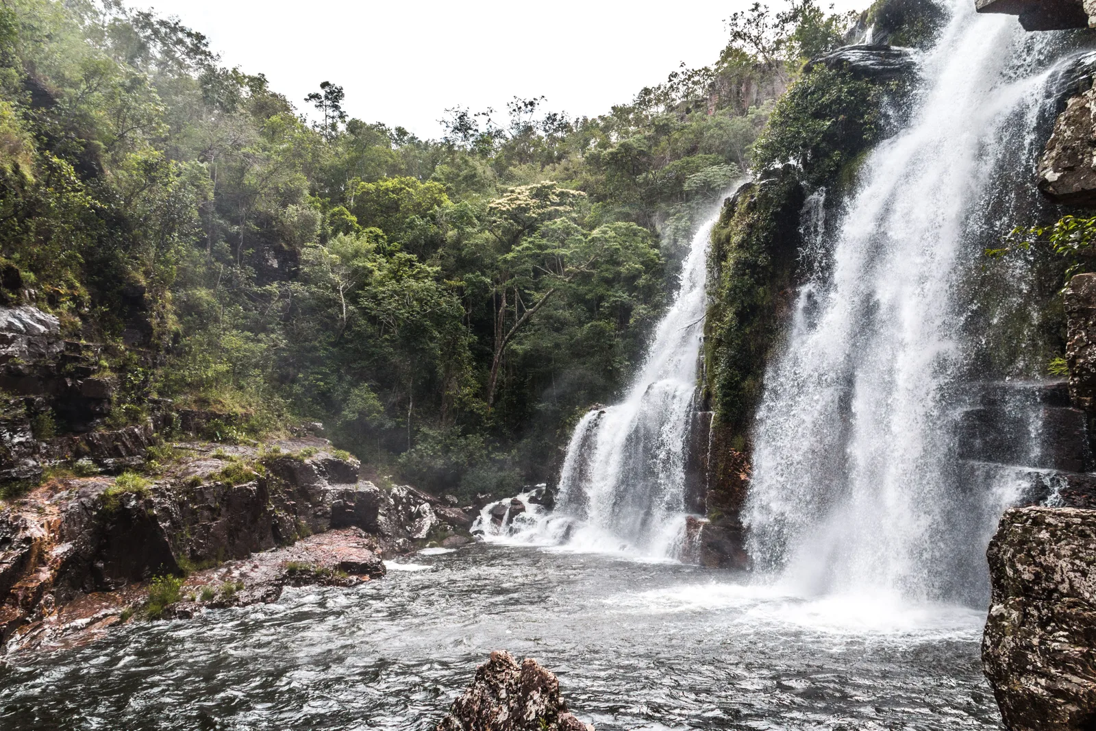 A waterfall dropping in several streams down a rock face into a pool surrounded by forest