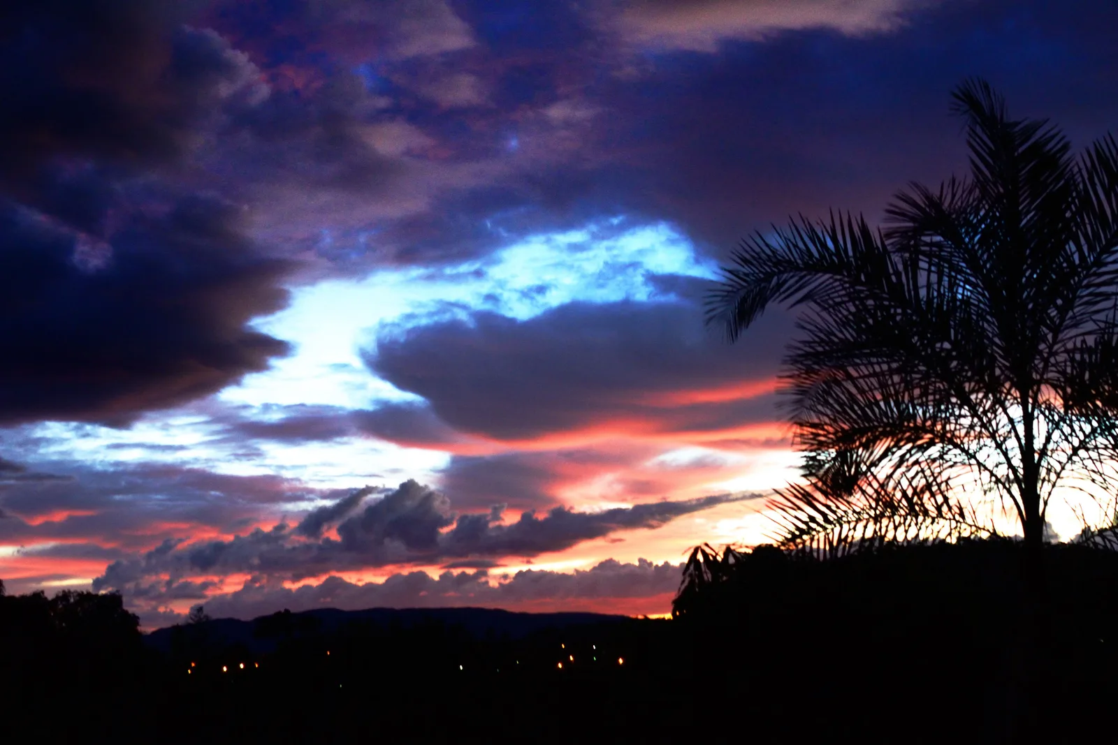 Dark clouds lit pink and blue above the black silhouettes of a palm and low hills near Cavalcante