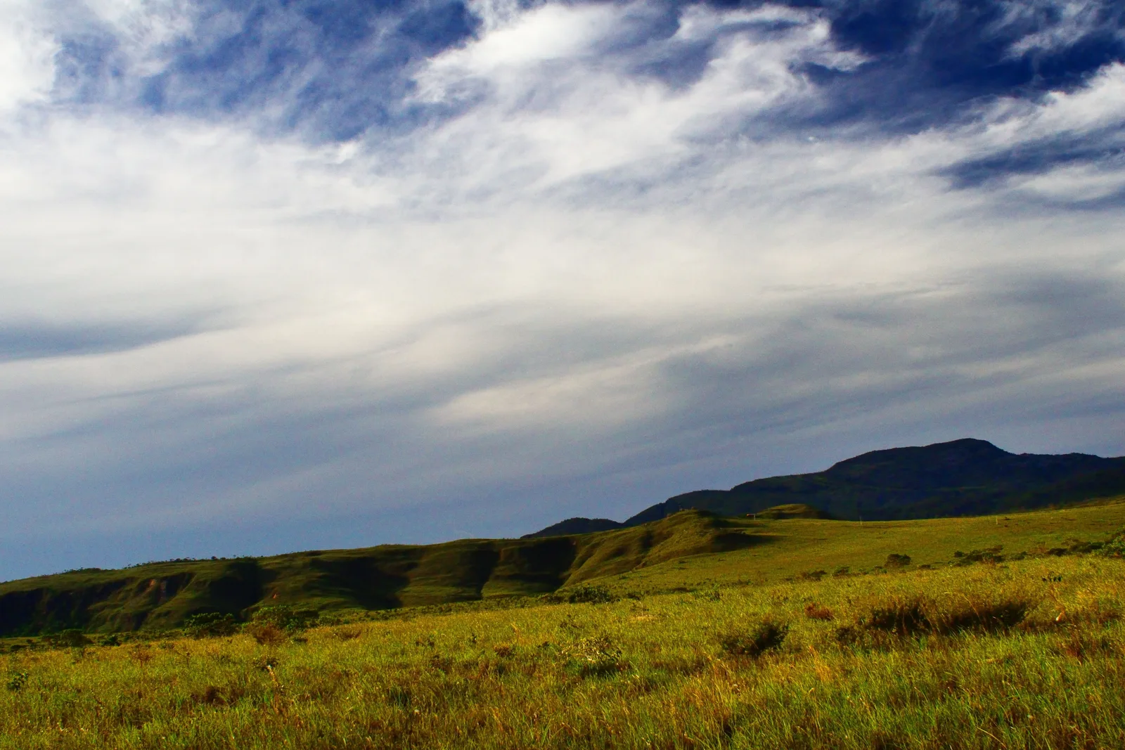 Streaks of white cloud over a green ridge and an open grassy slope on the plateau