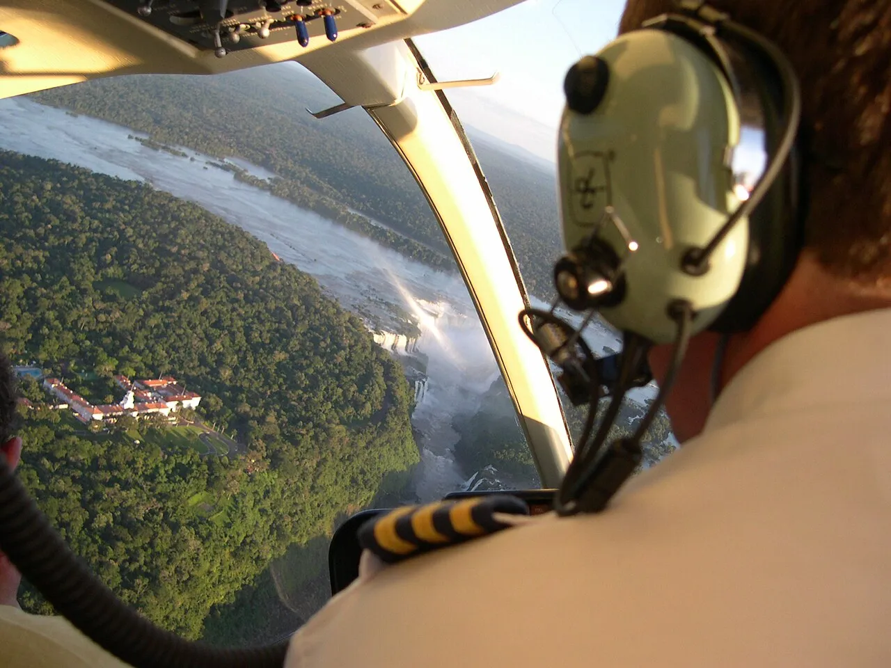 The view from inside a helicopter over Iguazu: the pilot’s headset filling one side of the frame and the falls and the river laid out through the windshield