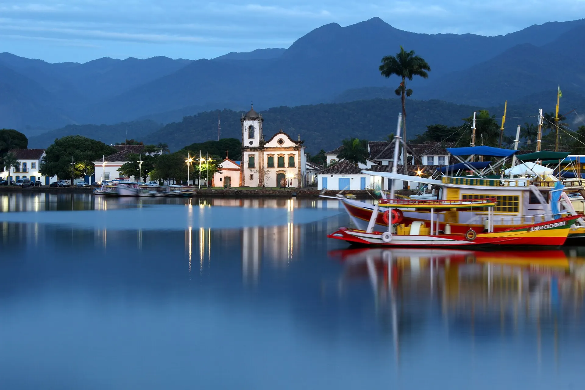 The whitewashed Santa Rita church on the Paraty waterfront with colorful fishing boats and forested mountains behind