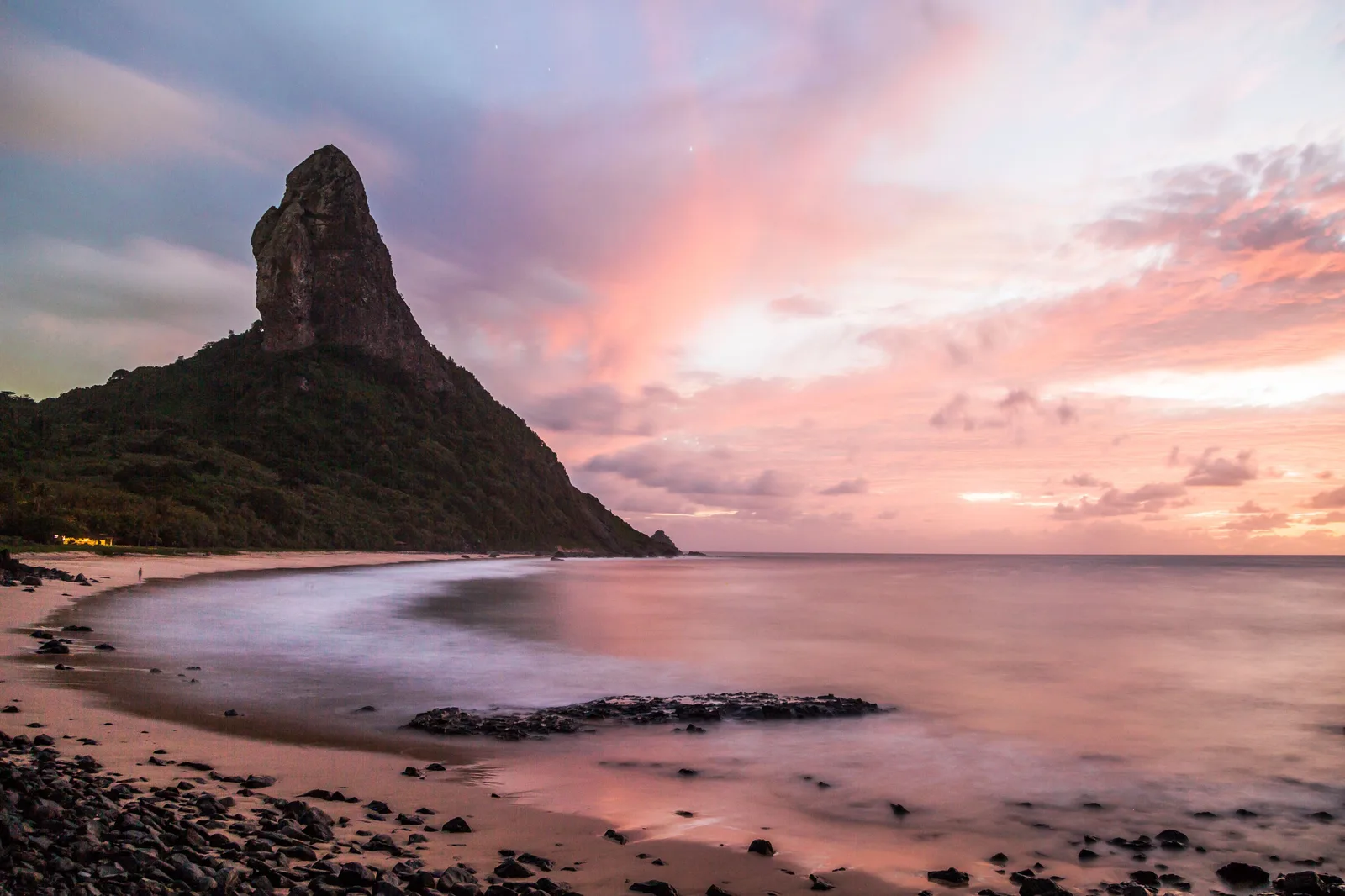 Morro do Pico standing dark against a pink and gray dusk sky above Praia da Conceição, with the wet sand and shallow water reflecting the light