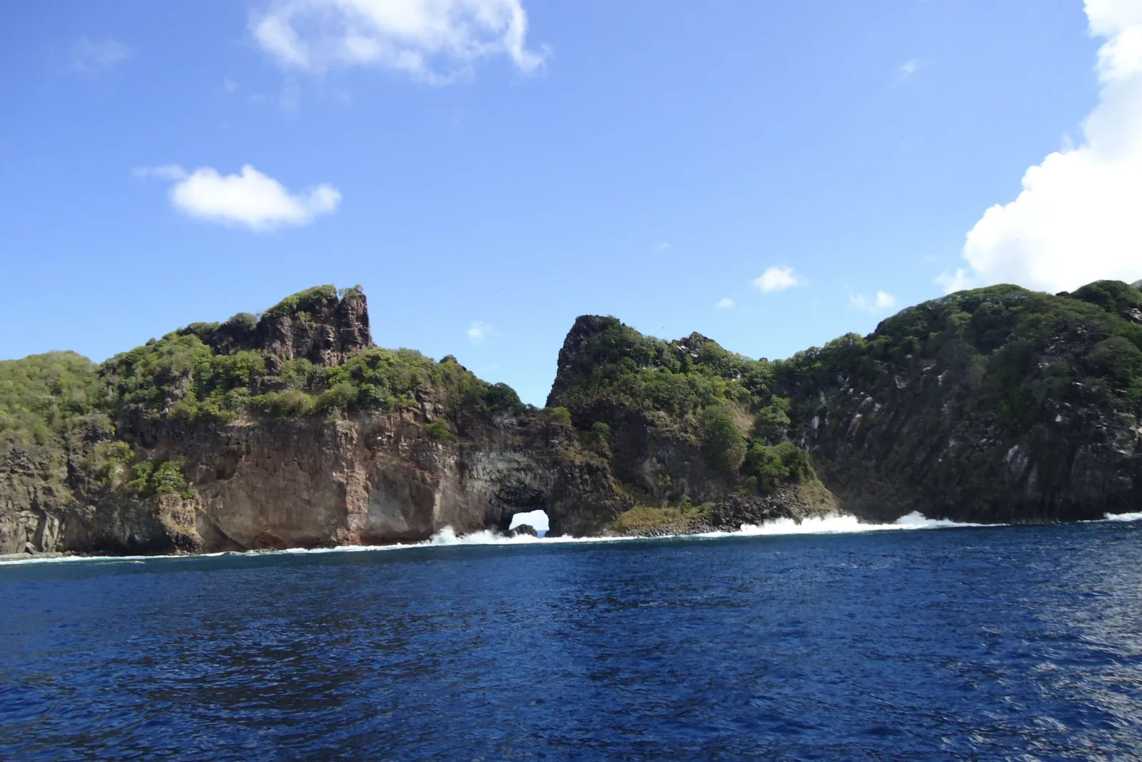 The cliffs at Ponta da Sapata seen from the water, with a natural rock arch punched through one headland and deep blue sea in the foreground