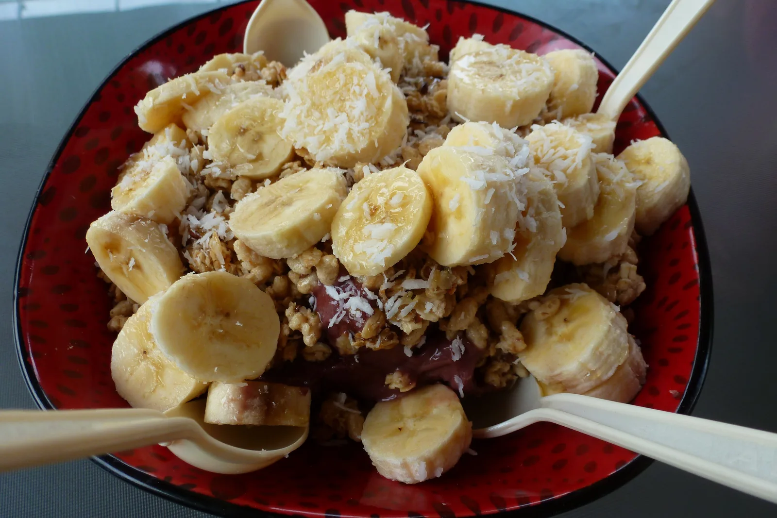 A bowl of thick purple açaí piled with banana slices, granola and shredded coconut