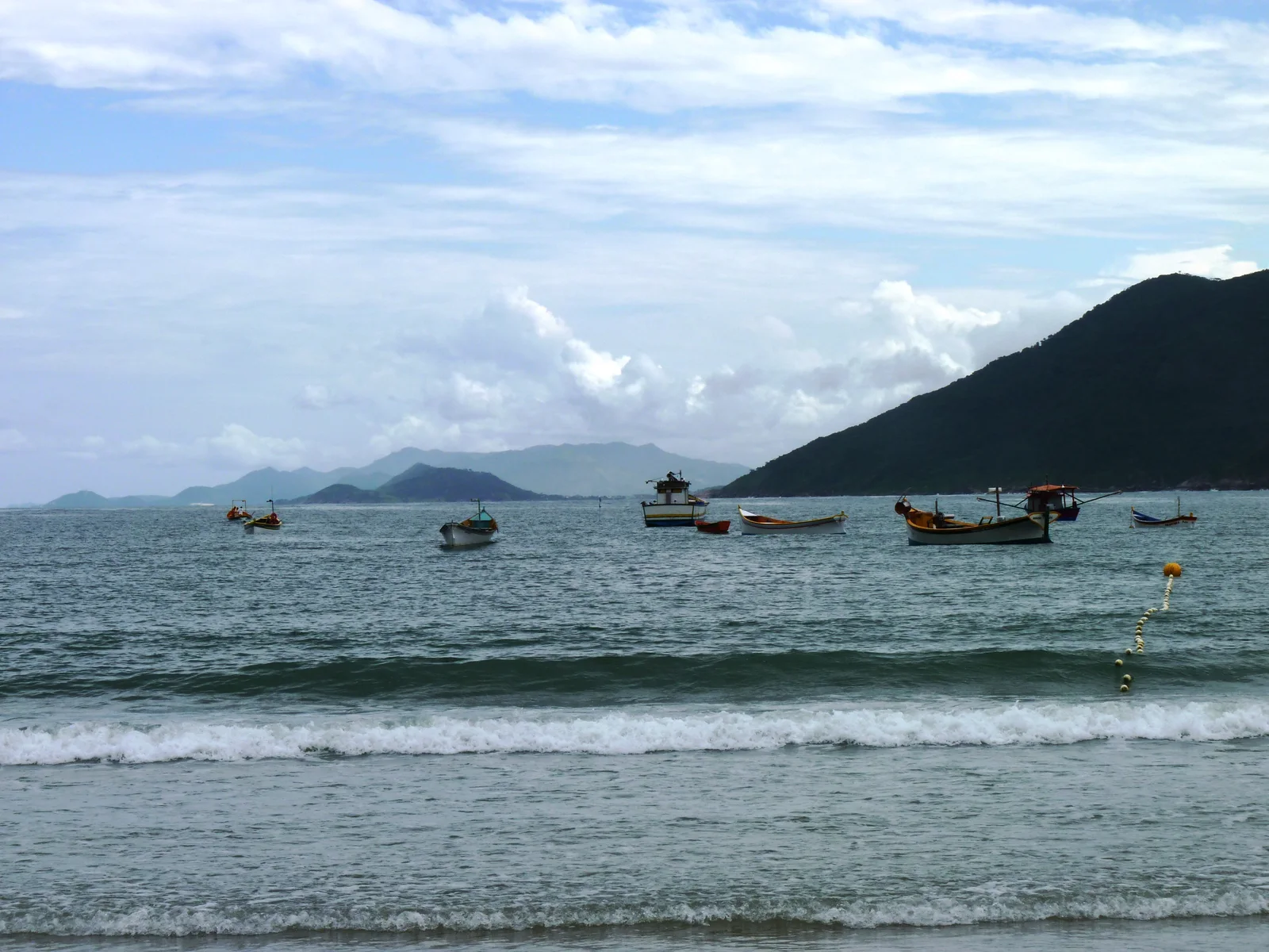 Fishing boats anchored off Praia da Armação, small waves running in and a green headland closing the bay