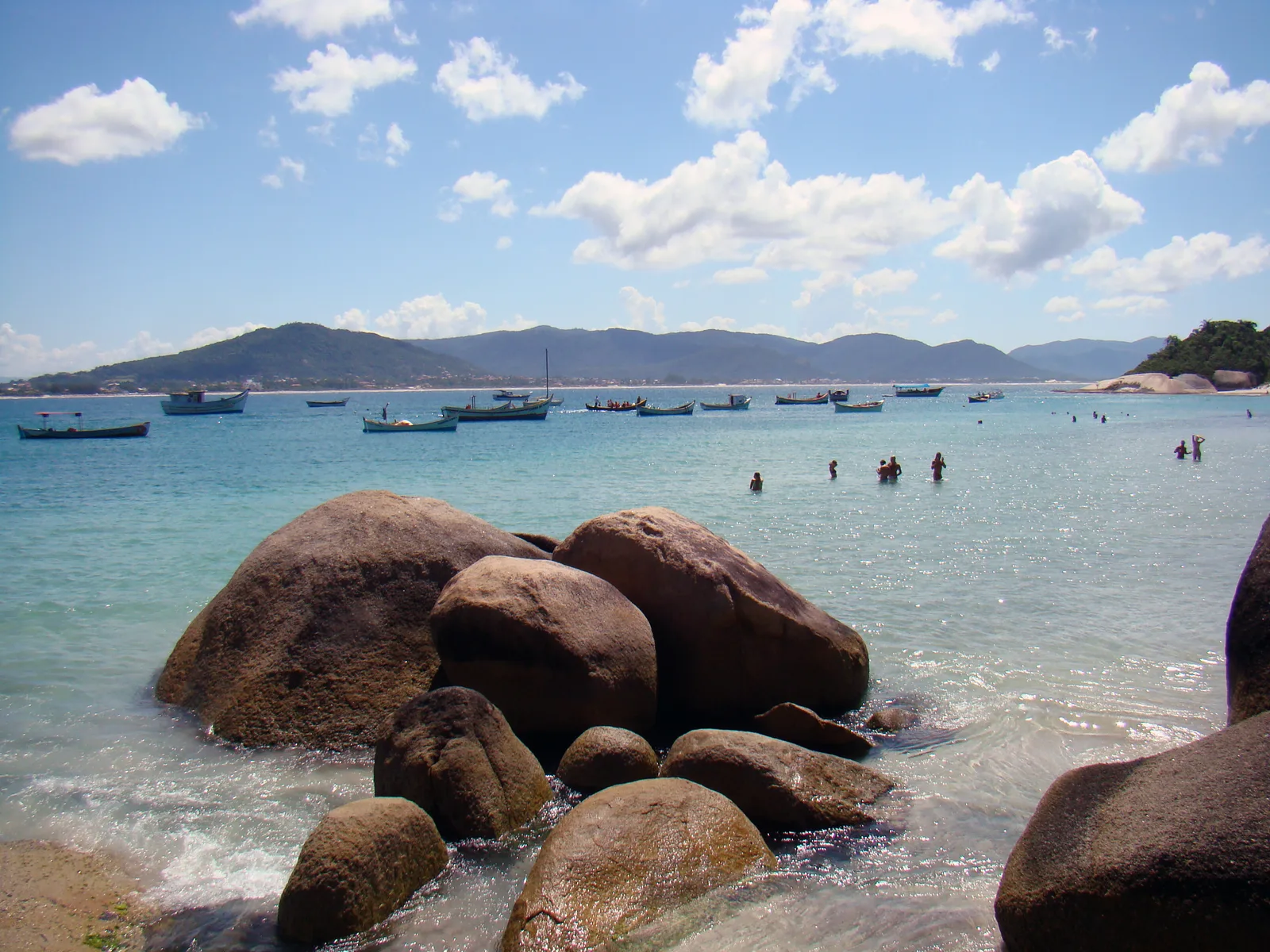 Clear turquoise water off Ilha do Campeche, granite boulders in the foreground and small boats anchored beyond