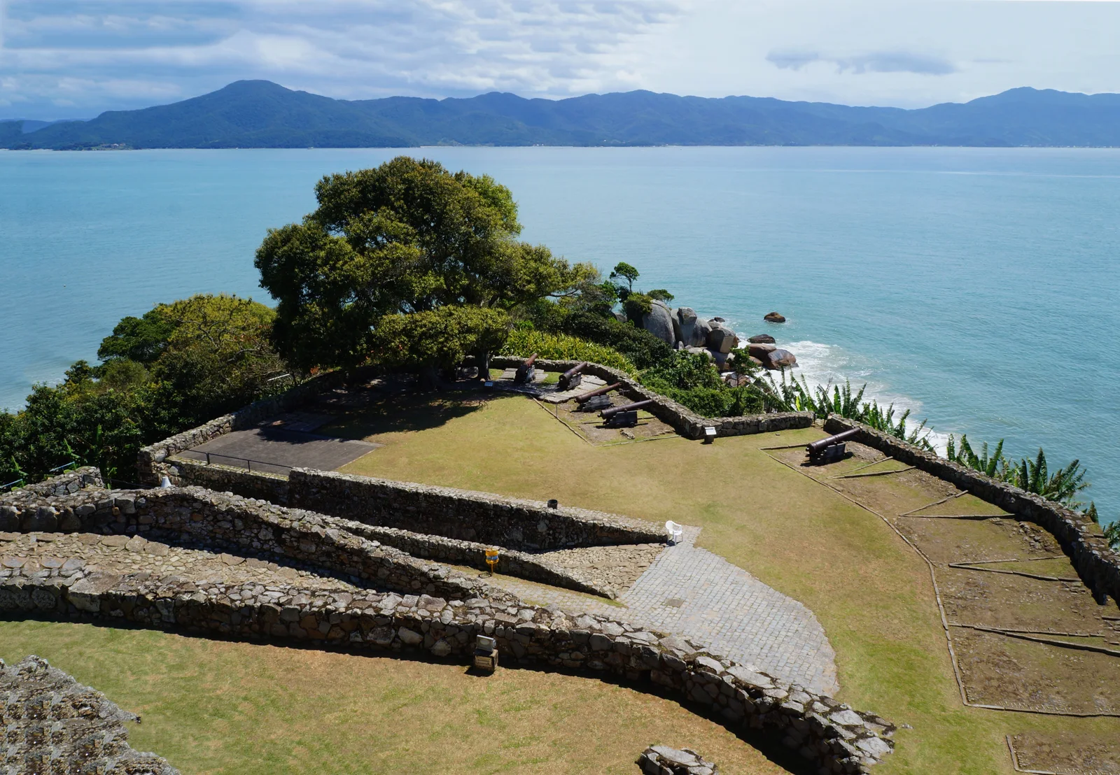 The stone ramparts of the 18th-century Fortaleza de São José da Ponta Grossa on its green point above the sea near Jurerê
