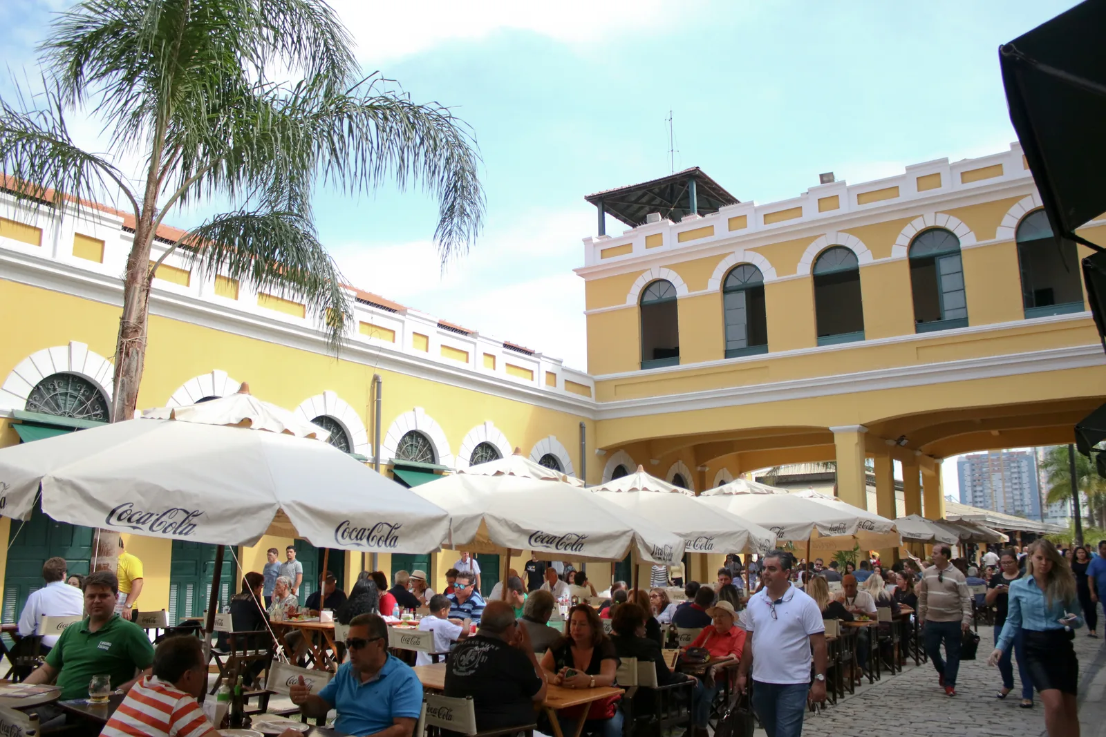 Busy lunch tables under umbrellas outside the yellow 1899 Mercado Público building in downtown Florianópolis