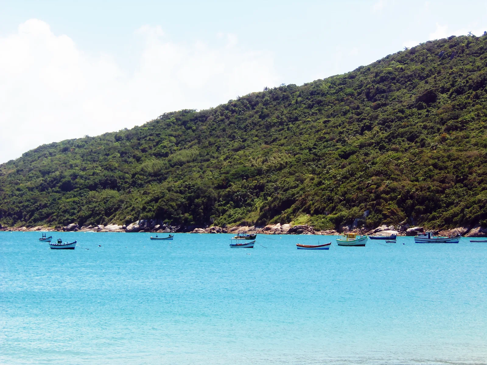 Small boats moored on brilliant turquoise water below the forested headland at Ponta das Canas