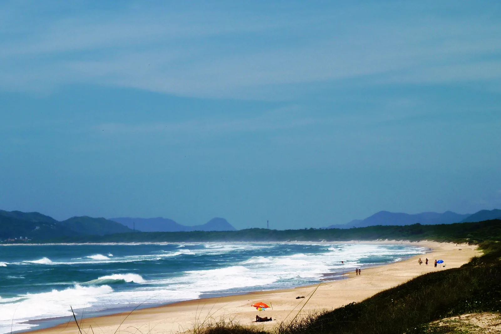 The long, empty stretch of Praia do Mocambique, vegetated dunes in the foreground, forested hills in the distance and no development in sight