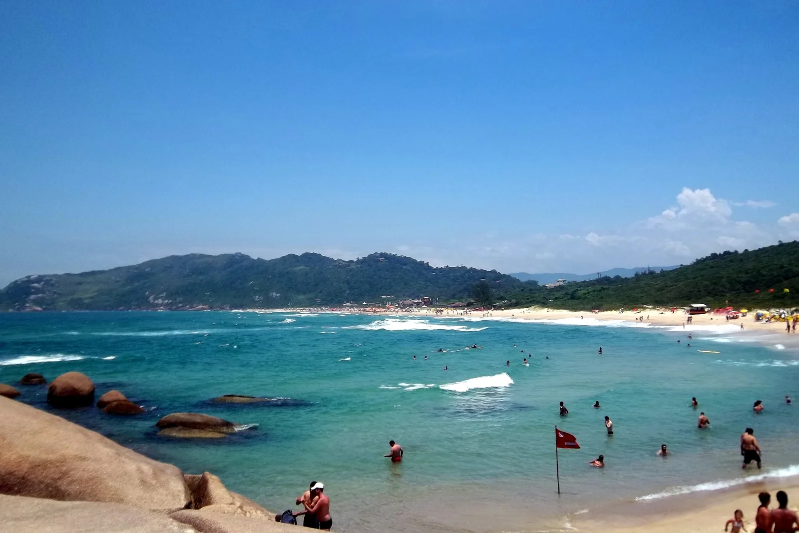 Turquoise water and granite rocks at Praia Mole on a sunny day, swimmers in the shallows and green headlands framing the beach
