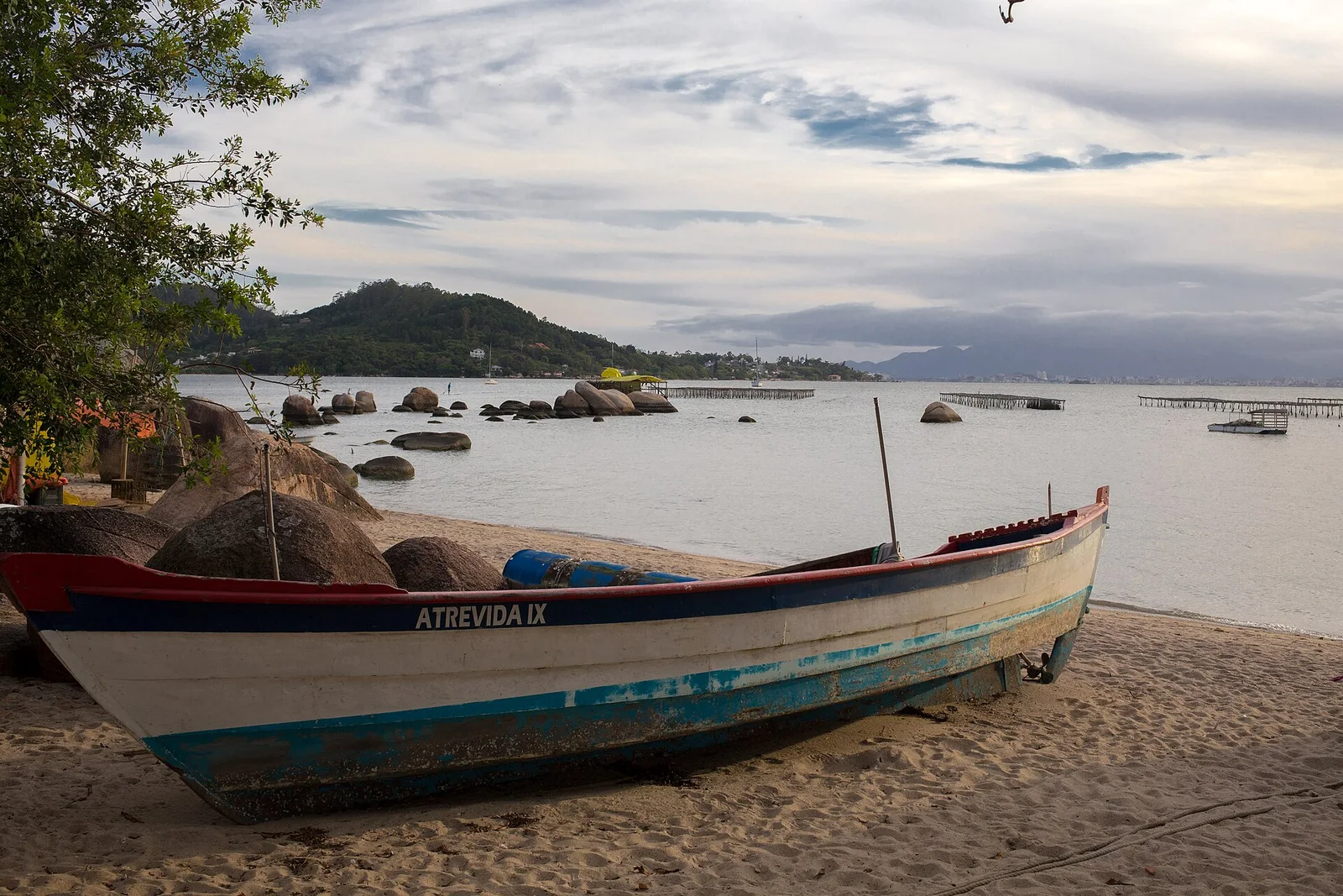 A wooden fishing boat drawn up on the sand at Santo Antônio de Lisboa, granite rocks and the calm bay behind it
