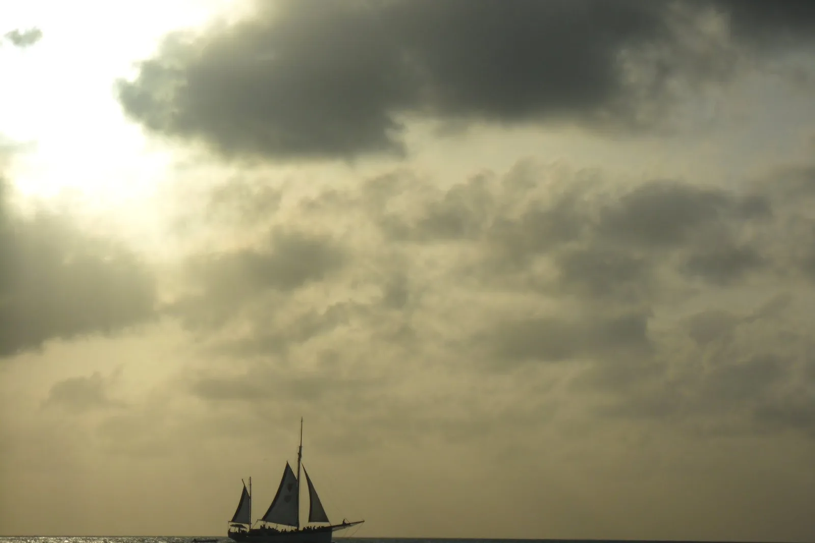 A two-masted schooner under sail, silhouetted against a golden, cloud-filled sky over the sea
