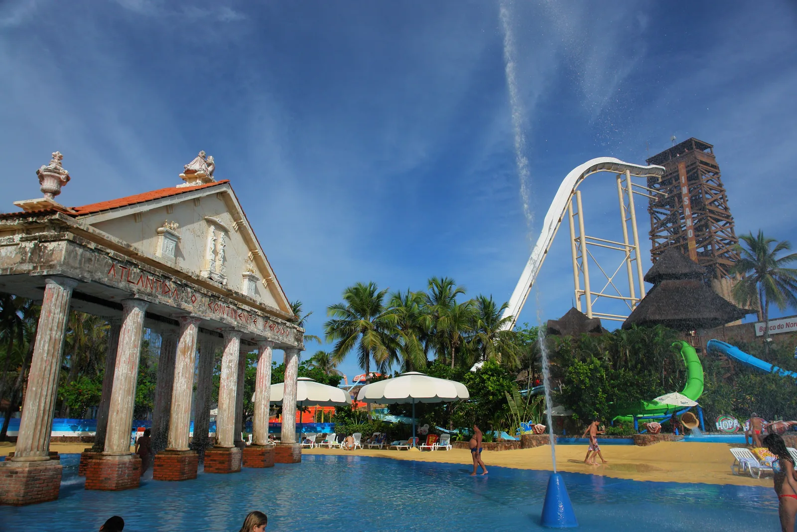 Beach Park water park at Aquiraz: a colonnaded white building beside a large pool, with a tall dark slide tower and a looping white water slide rising above the palm trees behind