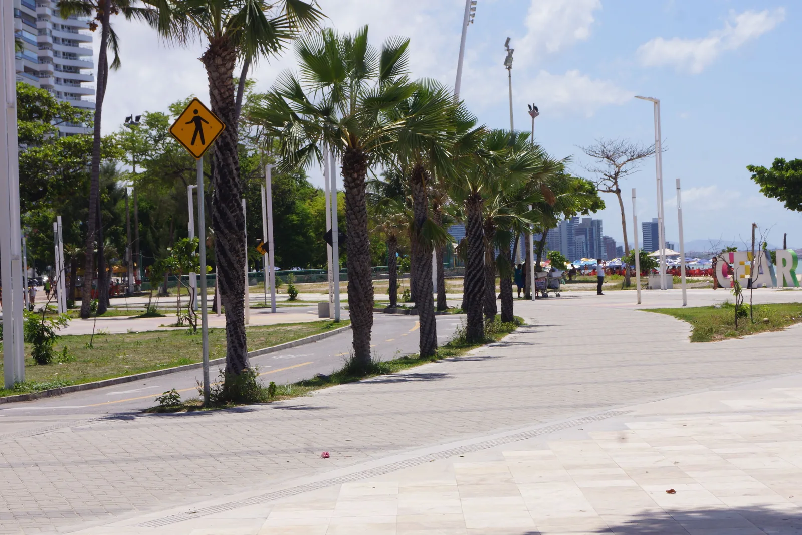 The rebuilt Beira Mar promenade in Fortaleza: a wide paved walkway with tall palms along its edge, a cycle lane beside it and the city towers in the distance