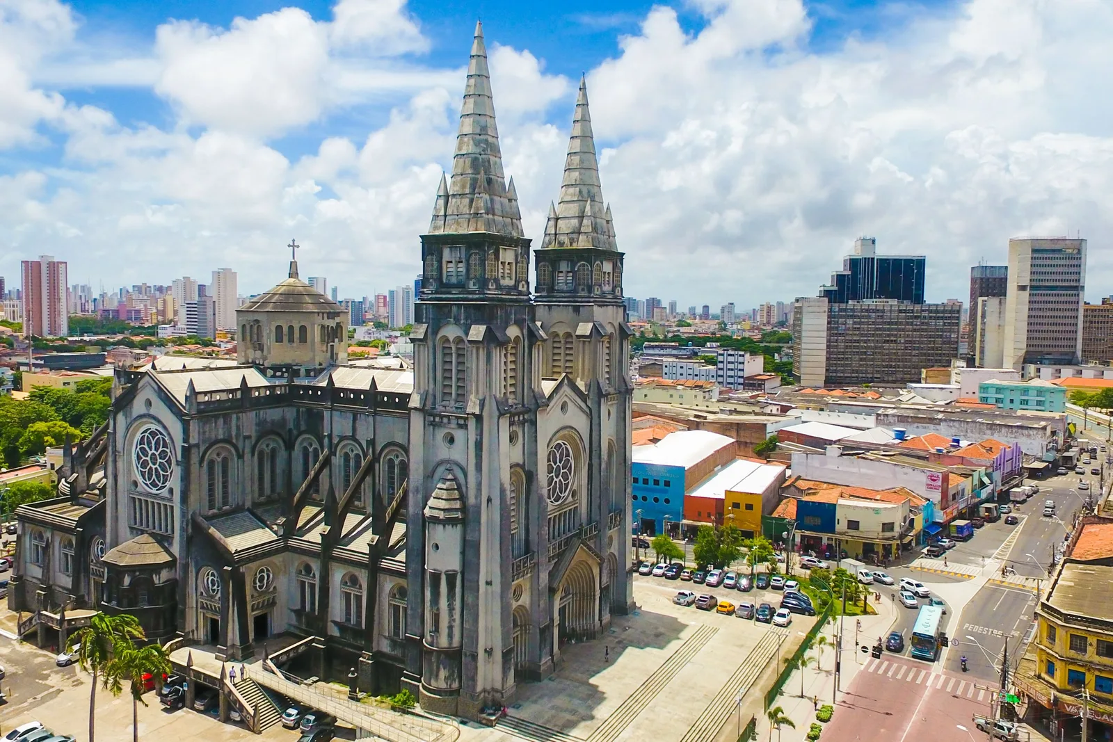 The Catedral Metropolitana de Fortaleza from the air: a gray twin-spired neo-gothic church rising above low red-roofed buildings, with the city towers behind it
