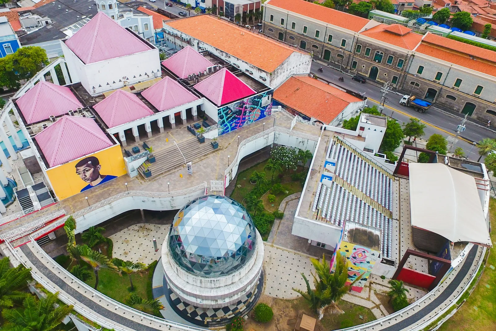 The Dragão do Mar cultural center from the air: a curved white building with a mirrored planetarium dome, pink-roofed colonial houses along one side and raised walkways linking the buildings