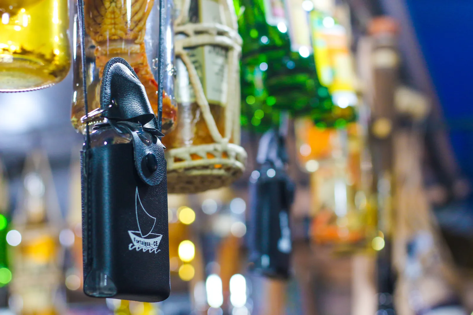 Bottles of cachaça and liqueur hanging in rows at a craft-fair stall, one dark bottle in focus in the foreground