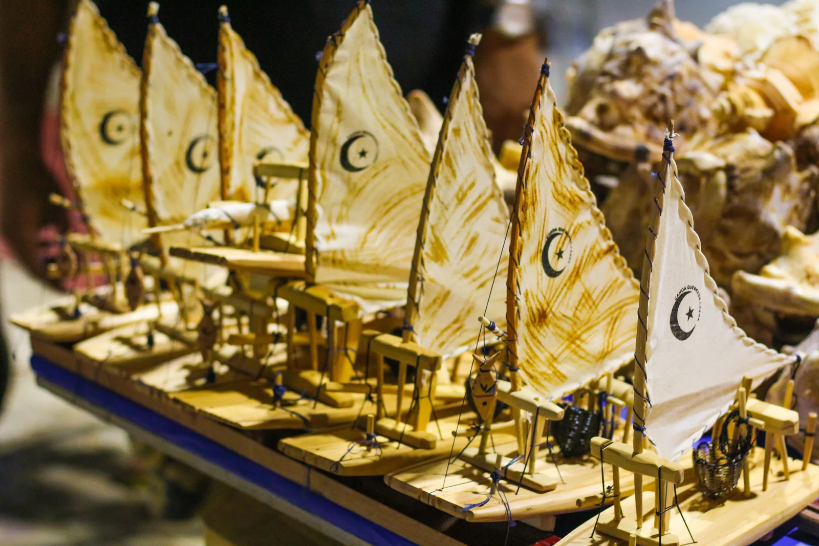 Model jangadas with cream cloth sails lined up on a souvenir stall, each one painted with a crescent moon and star