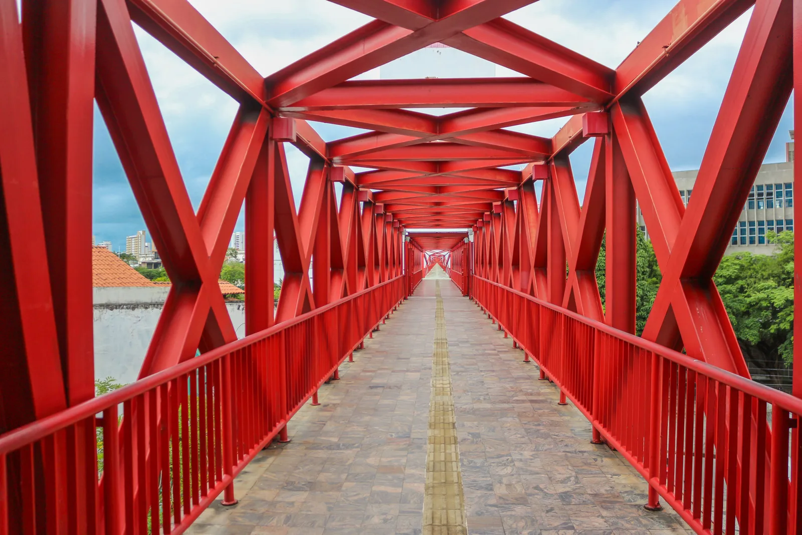 The red steel footbridge at the Dragão do Mar cultural center, its lattice frame running away from the camera like a tunnel with the city visible through the sides