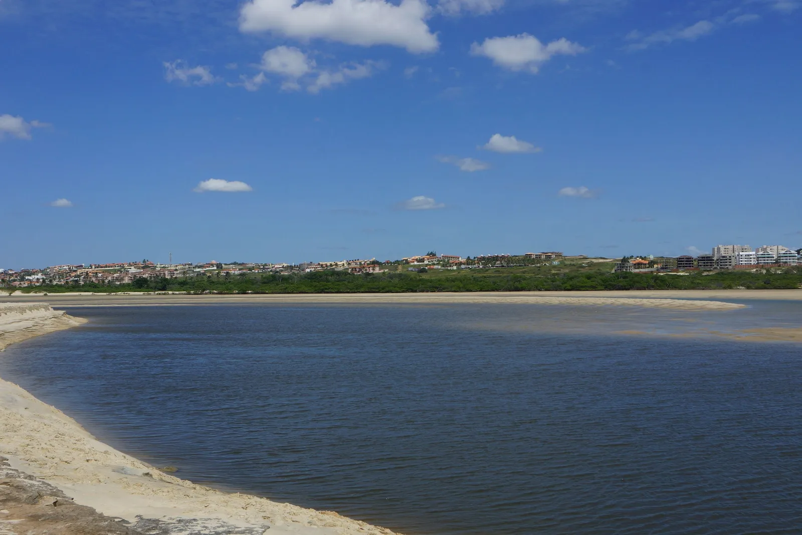 A wide brown river estuary at Aquiraz running out across a sandbar into the sea, with low green scrub along both banks