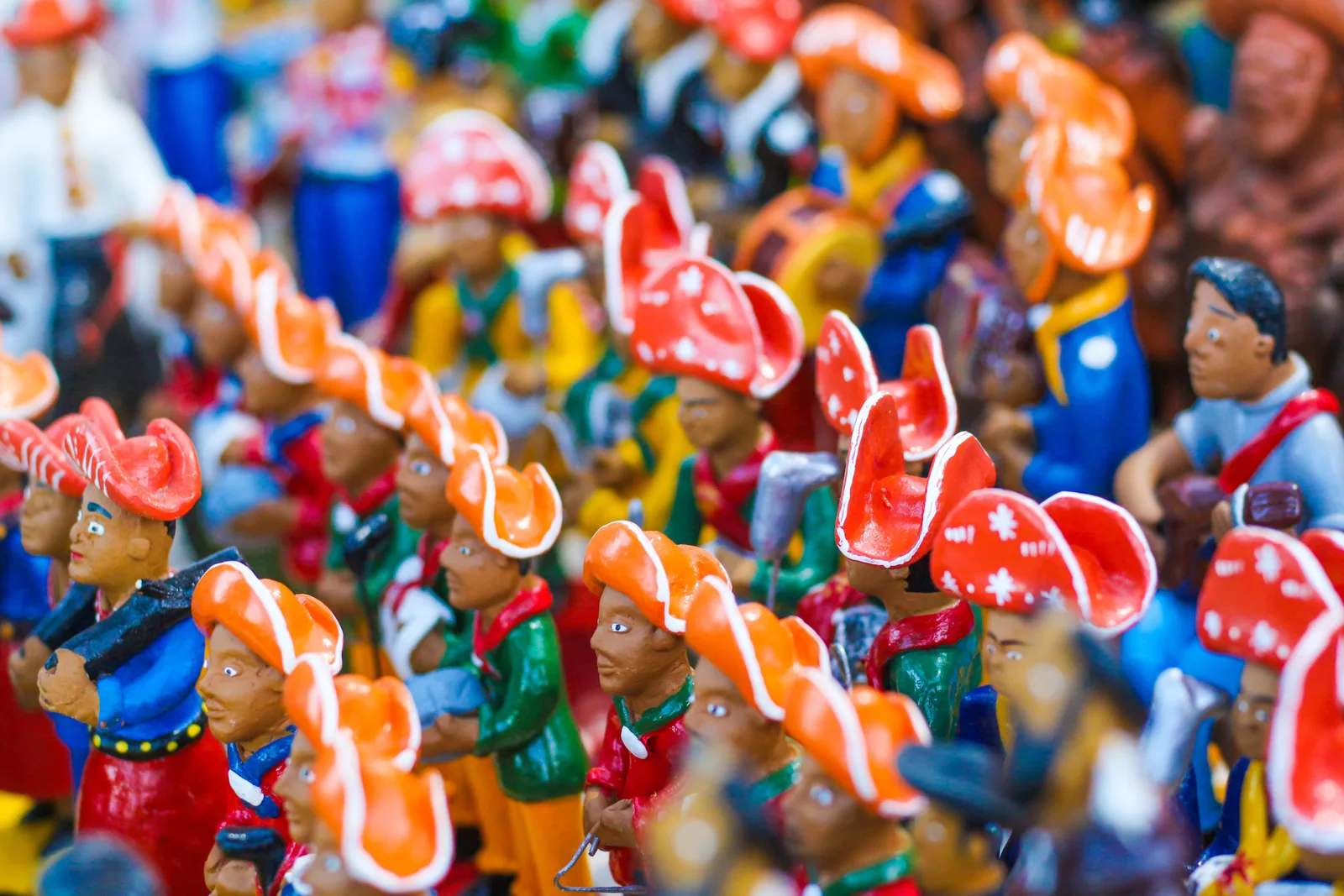 Rows of small painted clay figures in red leather hats crowded together on a craft-fair stall