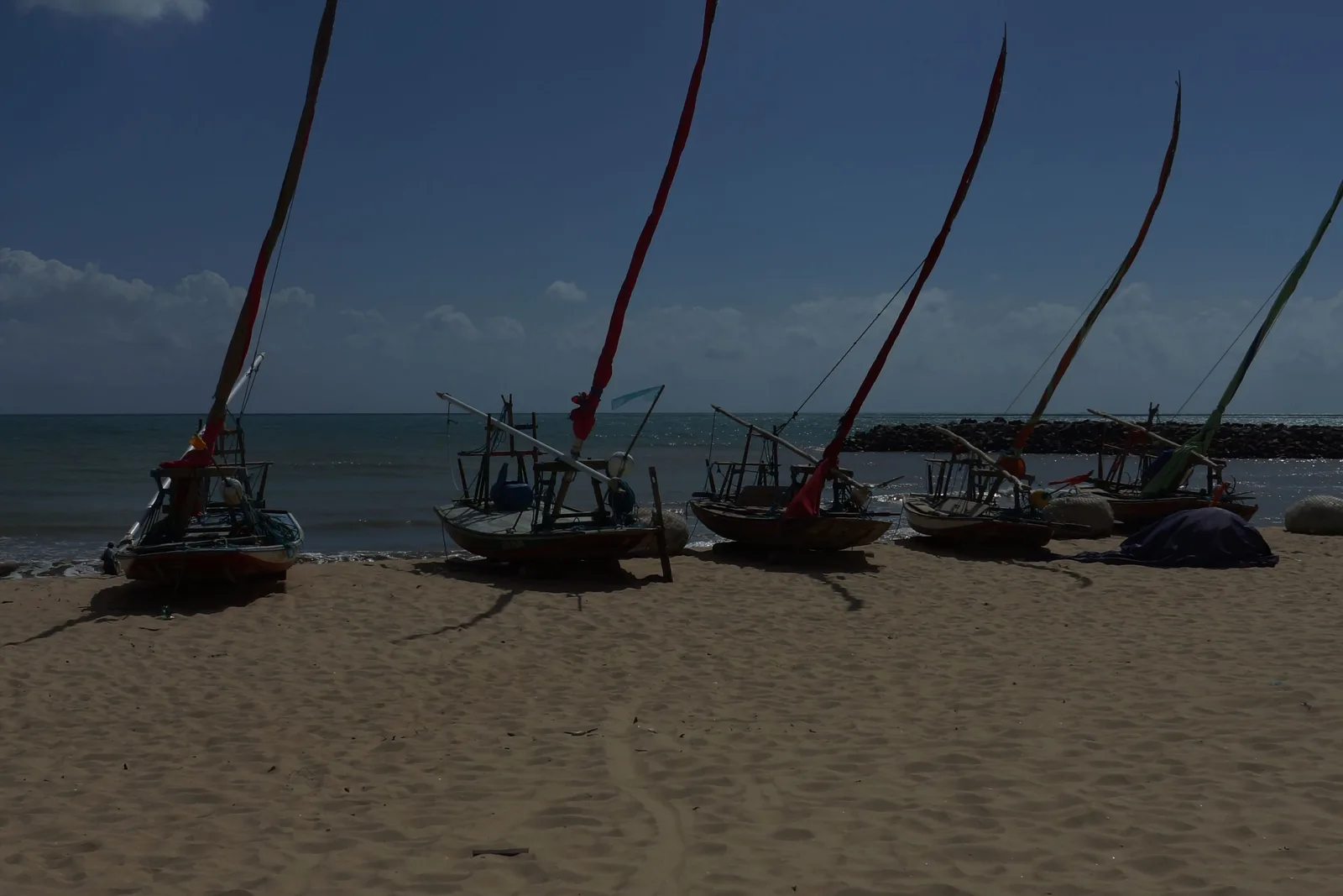 A line of jangadas drawn up on the sand with their tall masts raked back, the sea flat behind them