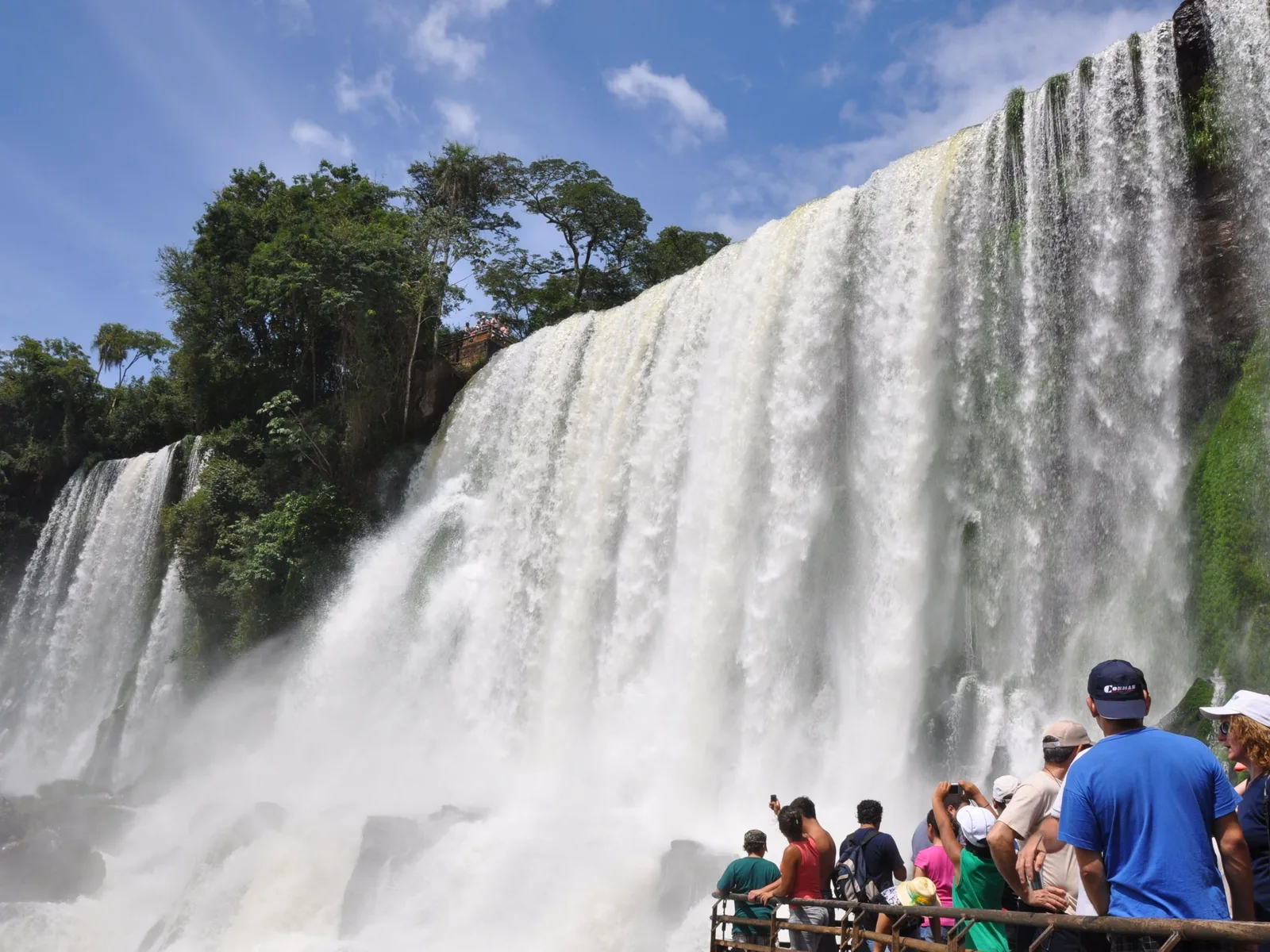 Visitors at a railed viewpoint on the Argentine Lower Circuit, a wall of water coming down immediately beside and above them and a second lookout small on the clifftop