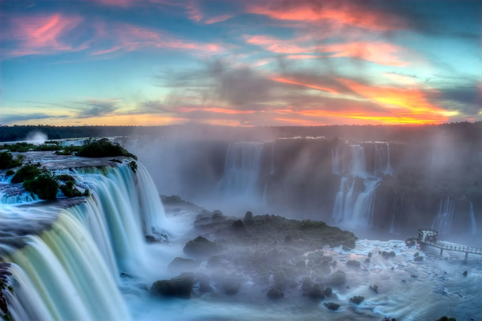 Iguazu Falls at sunset, the sky banded pink and blue above the spray and nobody in the frame