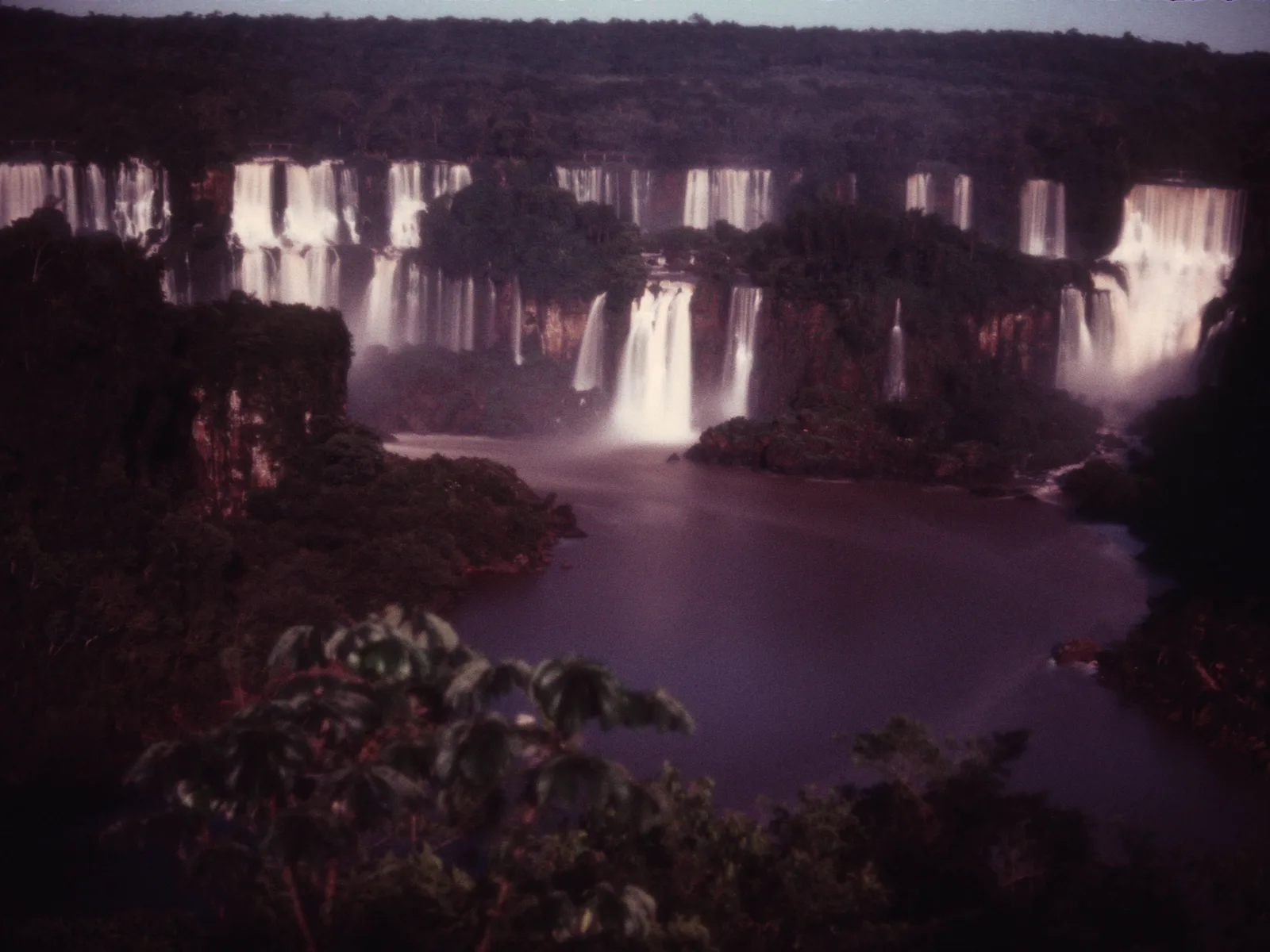 Iguazu Falls photographed at night, the long line of drops lit pale against the dark gorge