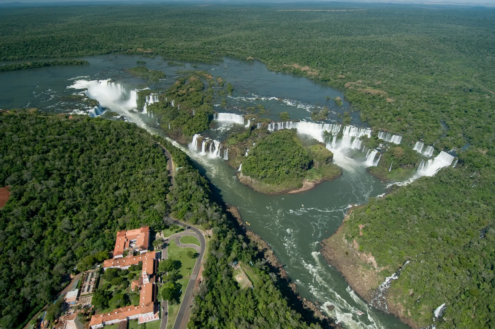 The falls from the air with the pink Hotel das Cataratas on the Brazilian rim and rainforest all around