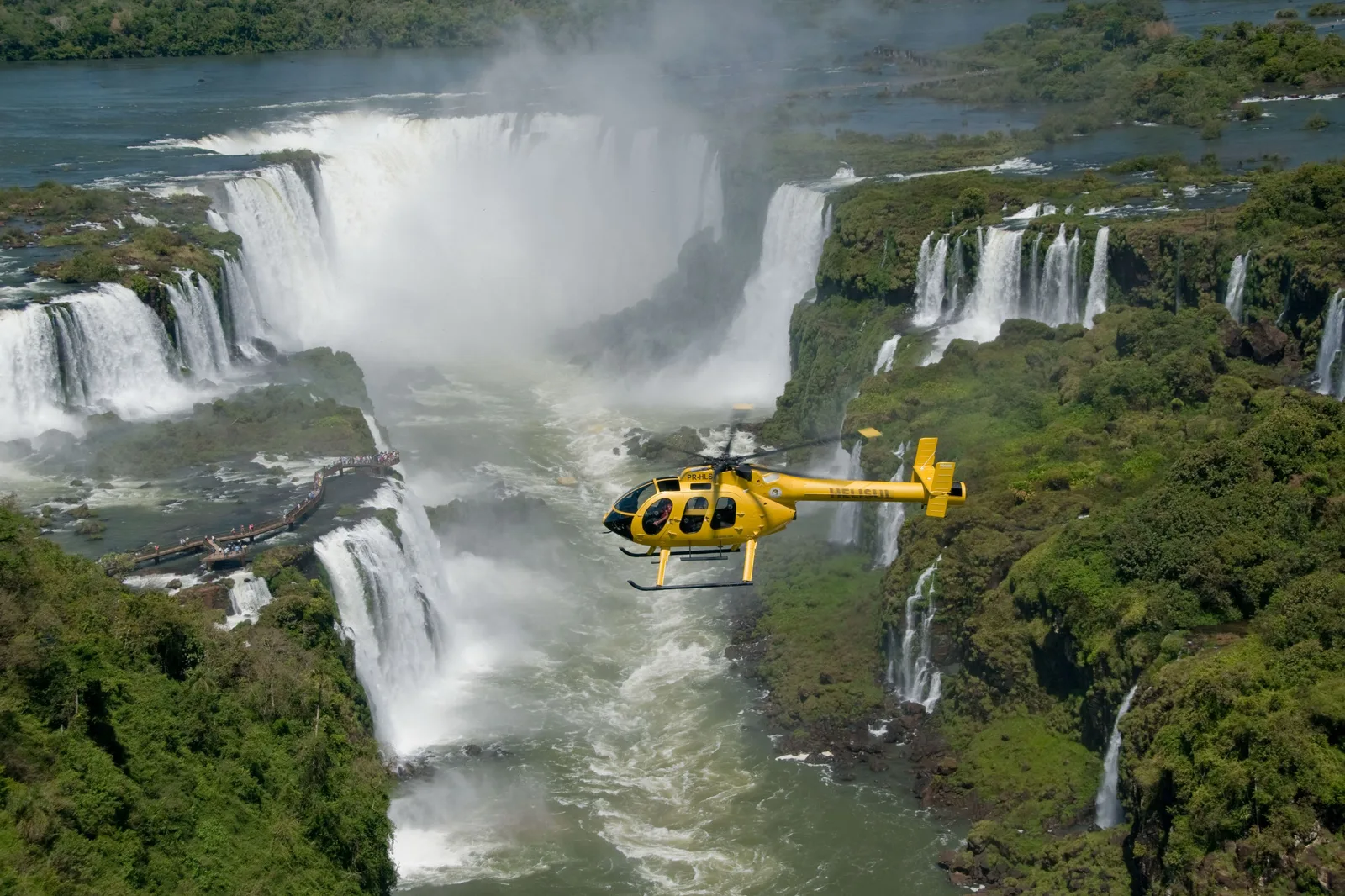 A yellow helicopter flying low over the falls and the river canyon