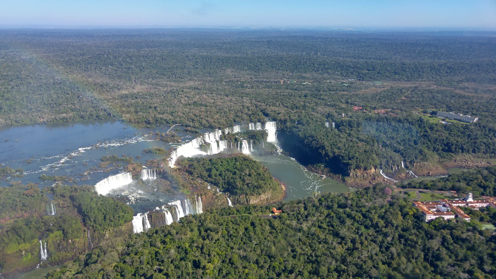Iguaçu Falls from the air, the whole line of drops curving through rainforest