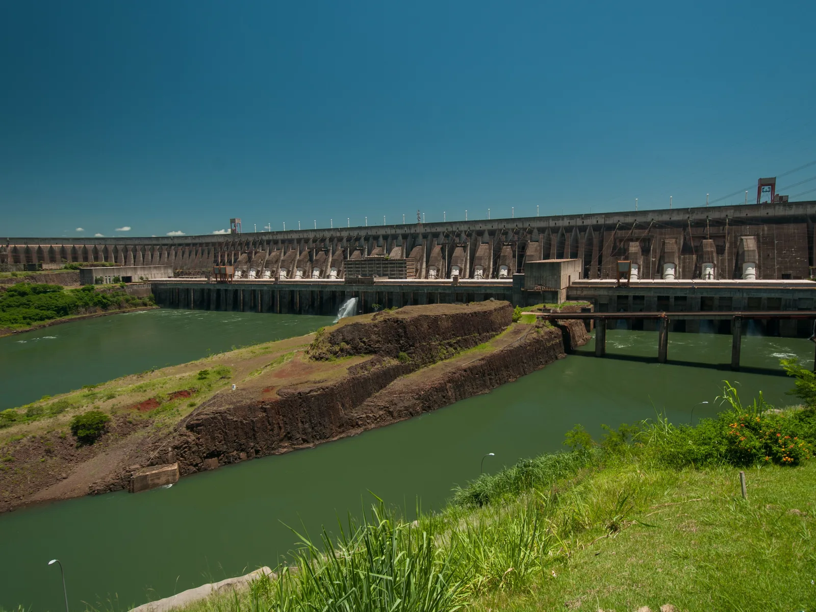 Itaipu seen from downstream: the buttressed concrete face and the powerhouse running the full width of the frame, with the green tailrace channel below