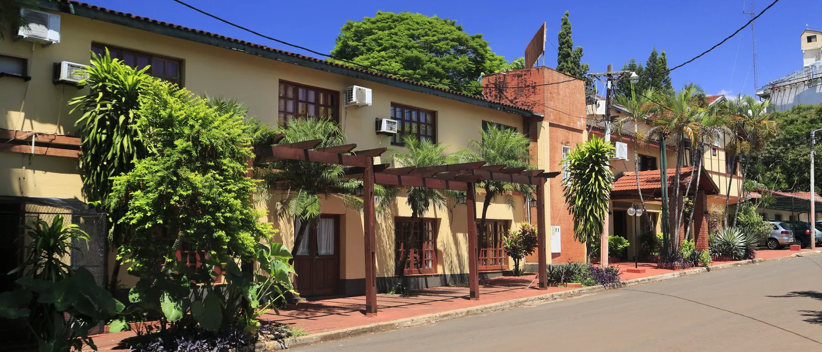 A quiet low-rise street in Puerto Iguazú, red-tiled roofs and heavy greenery on both sides and no traffic on it