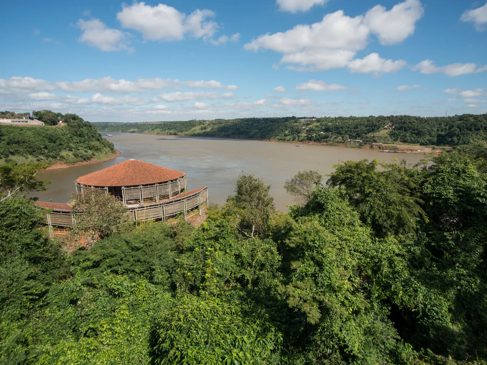 The Iguaçu and Paraná rivers meeting below the Marco das Três Fronteiras, the landmark’s round roof on the bluff and forest running down to the water