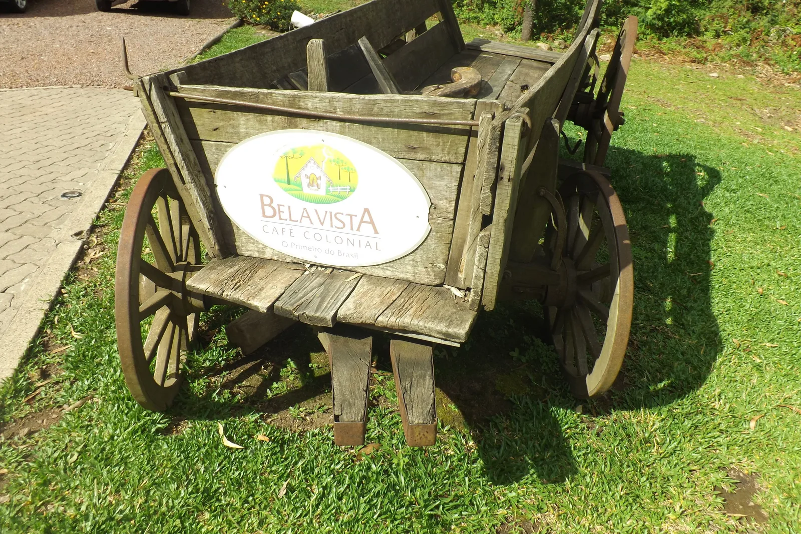 An old wooden farm cart on a lawn with an oval sign for the Bela Vista café colonial fixed to its side