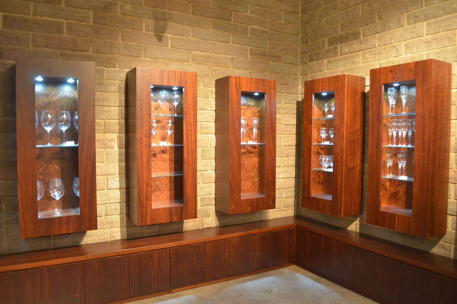 Lit wooden display niches holding wine glasses set into a pale brick wall at Casa Valduga