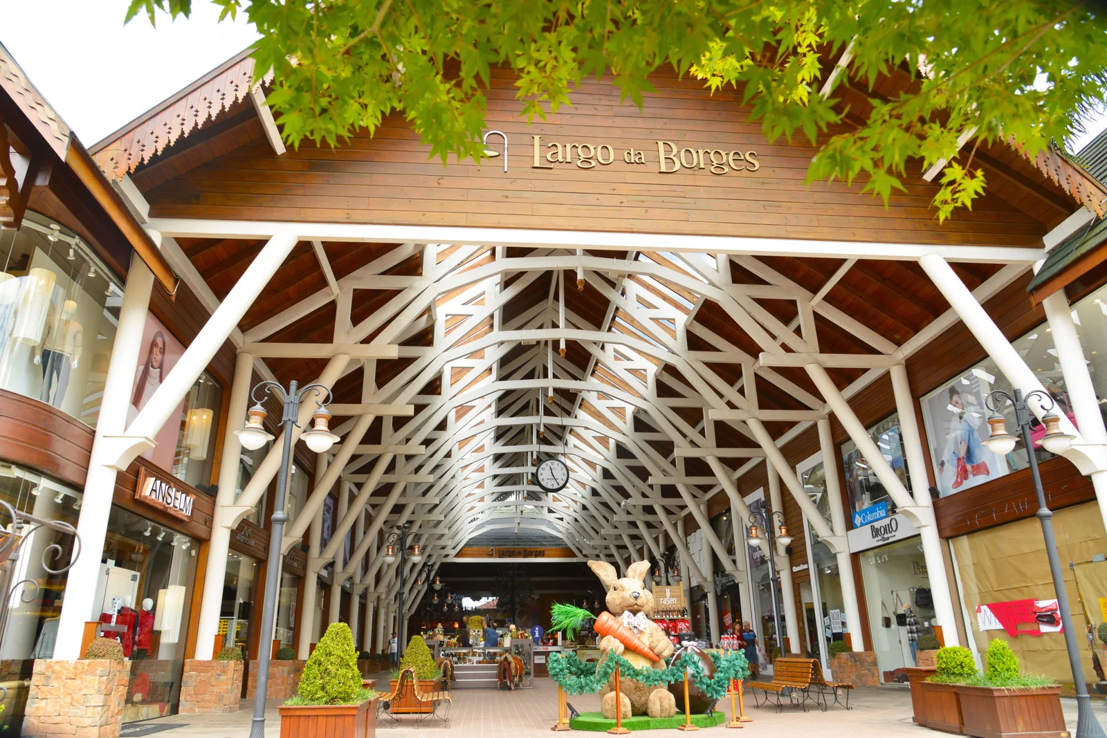 The entrance to the Largo da Borges arcade in Gramado: a wooden gable with the name in gold letters over a white timber-framed roof, shops on both sides and an Easter rabbit figure at the far end