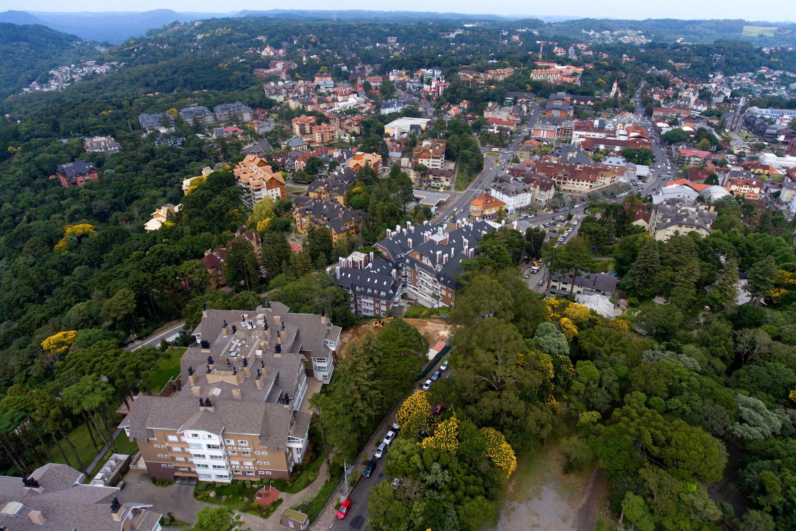 Gramado from the air: red roofs, apartment blocks and church spires among trees, with the town running off toward the hills
