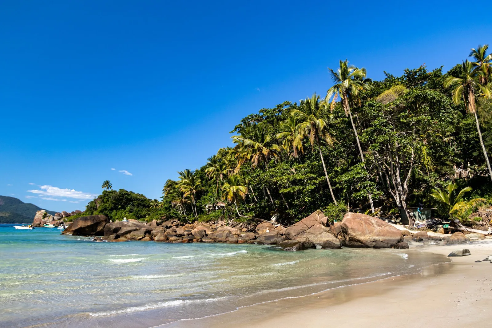 A small cove of pale sand and very clear shallow water, palms leaning over granite boulders at one end