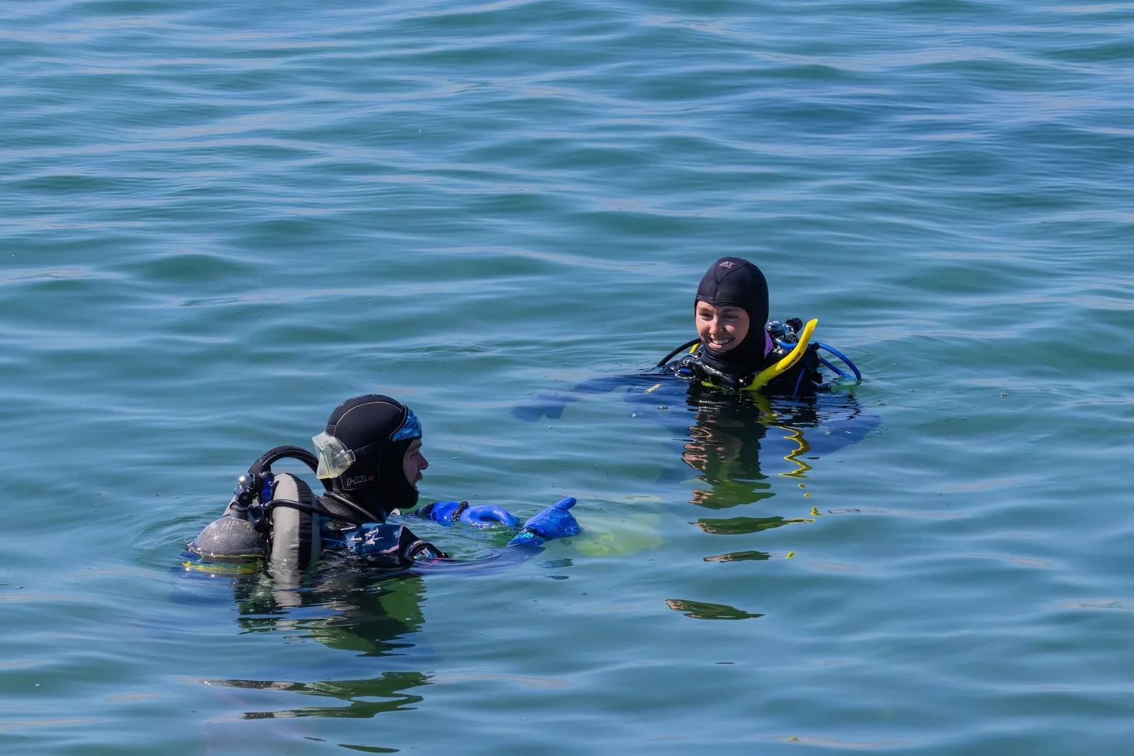 Two divers in wetsuits at the surface in clear shallow water