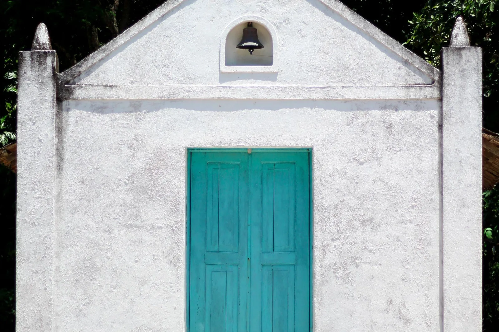 A small whitewashed island chapel with a turquoise door and a bell above the gable