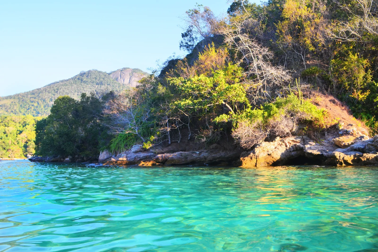 The clear turquoise shallows of the Lagoa Azul around a small rocky islet covered in forest