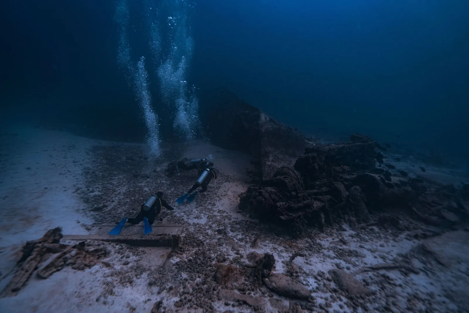 Two divers over the hull of a sunken wreck, light coming down through green water