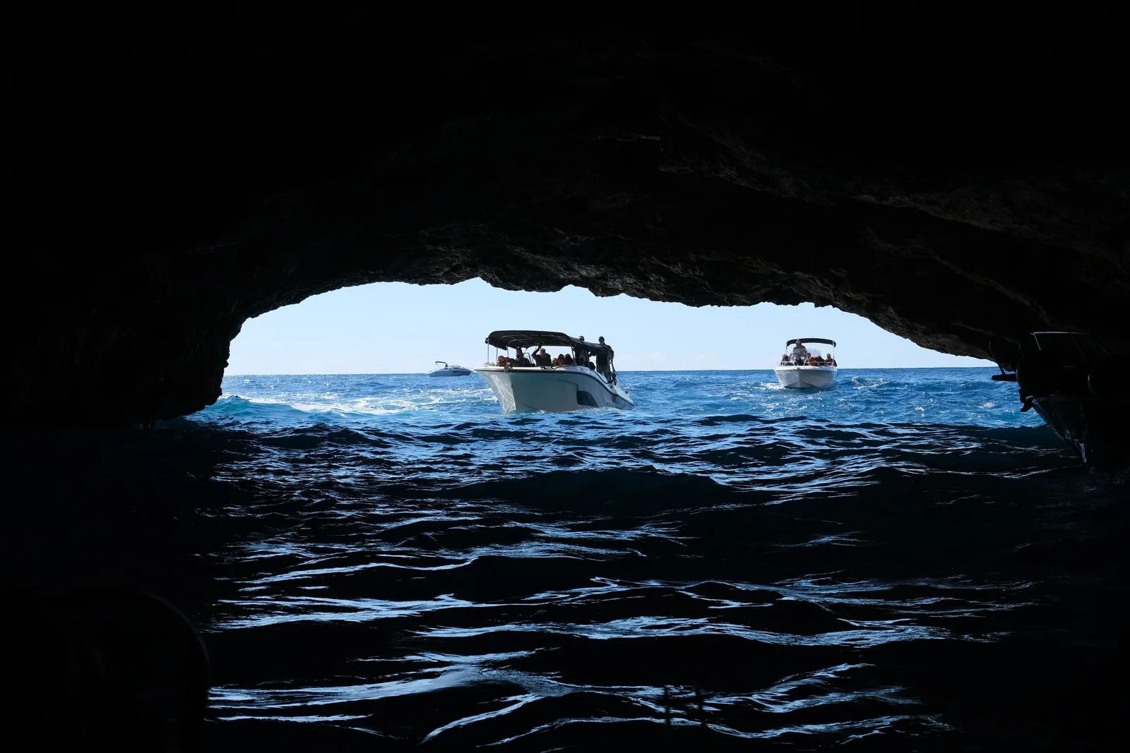 Small boats passing into a sea cave through a dark rock opening