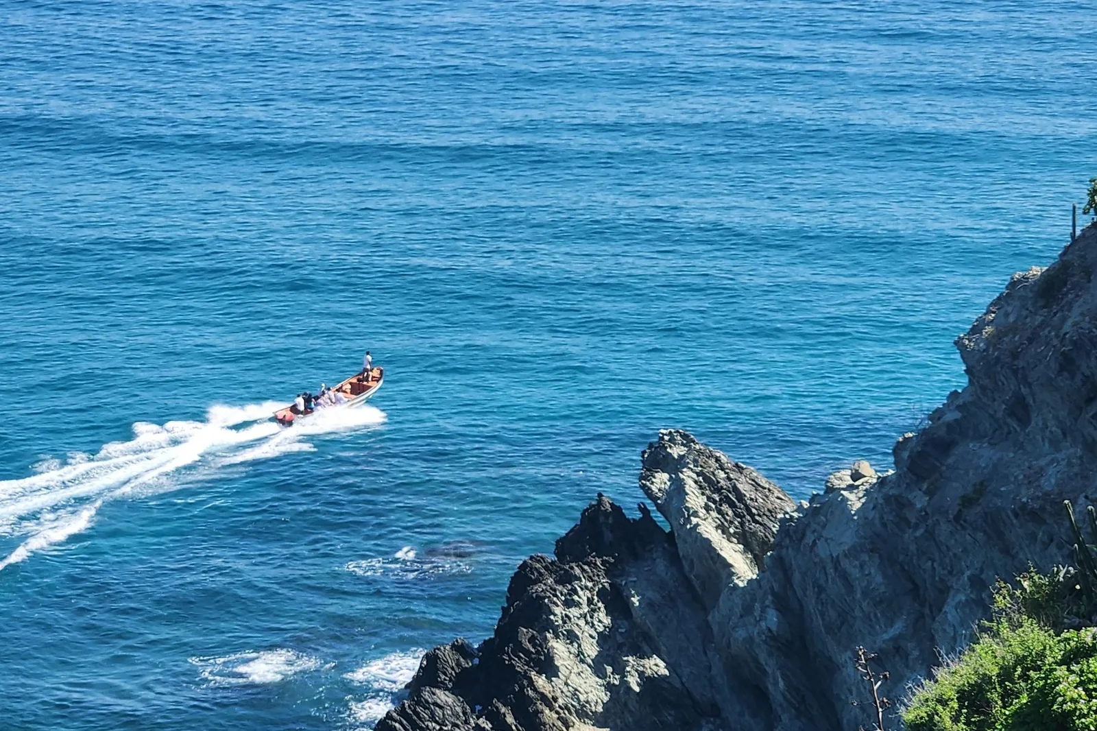 A fast open boat crossing clear blue water below a steep rock headland